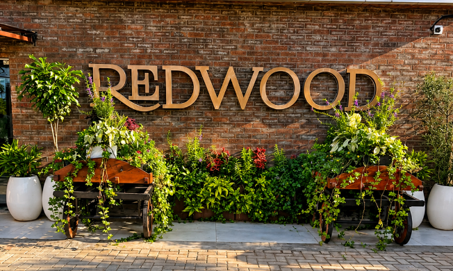 The REDWOOD sign on a brick wall framed by plants